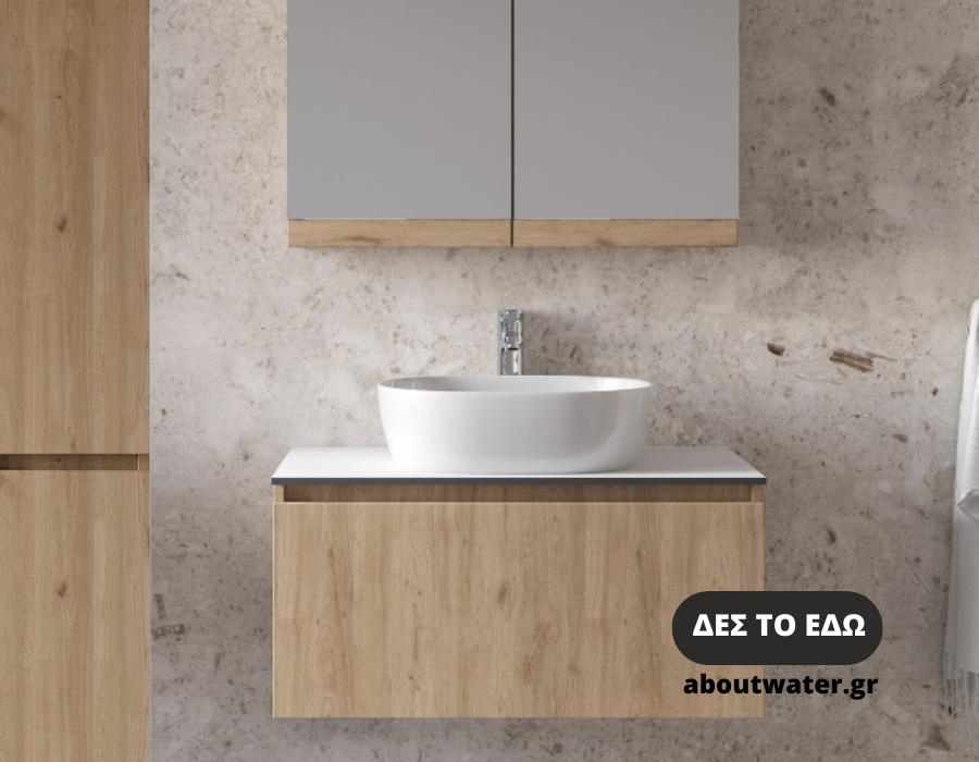 Έπιπλο μπάνιου με 2 συρτάρια και αριστερά στήλη μπάνιου με 2 ντουλάπια σε φυσικό χρώμα ξύλου και τα δύο. Το έπιπλο έχει λευκό πάγκο και πάνω λευκό επικαθήμενο νιπτήρα πορσελάνης και inox βρύση νιπτήρα. Πάνω από το έπιπλο υπάρχει καθρέφτης κρυφοντούλαπο. Το έπιπλο μπάνιου συνδυάζεται με πατητή τσιμεντοκονία στον τοίχο του μπάνιου.