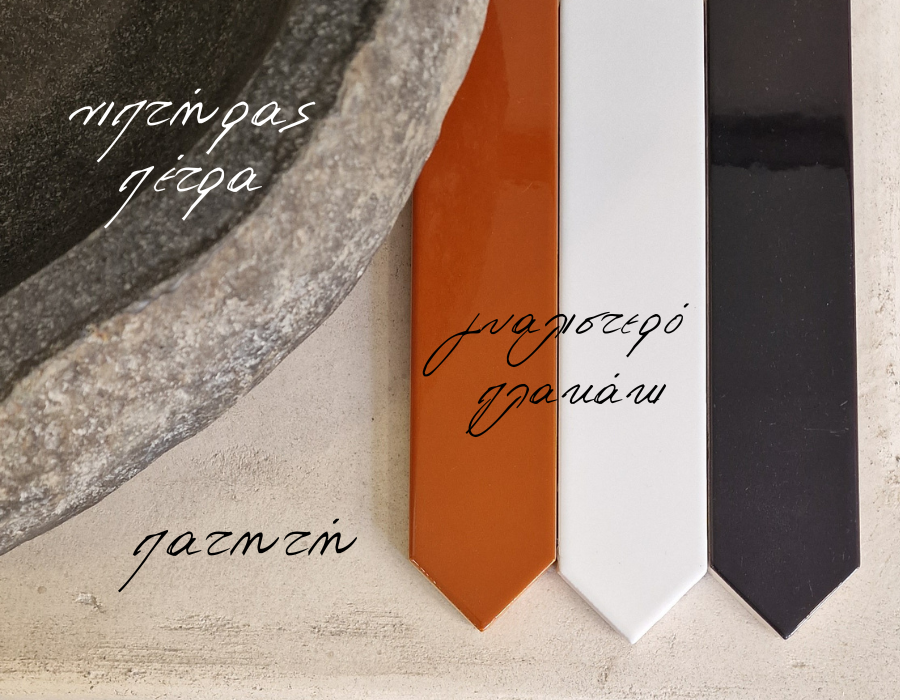 νιπτήρας από φυσκιή πέτρα πάνω σε πάγκο πατητής τσιμεντοκονίας και δίπλα 3 γυαλιστερά πλακάκια βέλος, λεπτά, μακρόστενα, σε μάυρο χρώμα, άσπρο και πορτοκαλί.